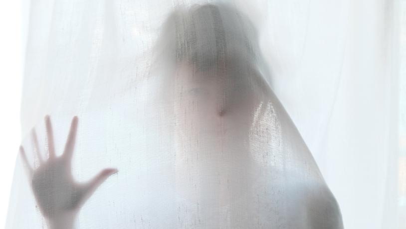 Spøgelseslignende form ses bag et hvidt gardin.