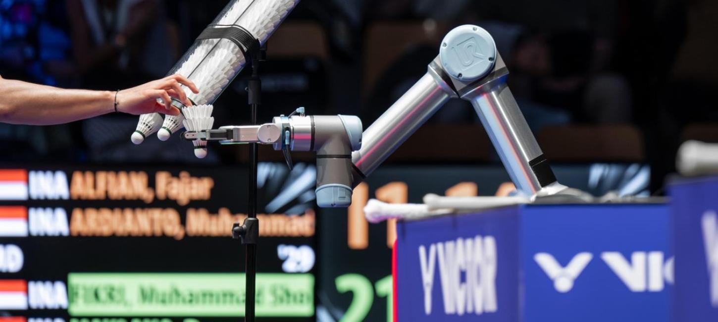Arm rækker ind i billedet og tager fjerbold fra robotarm badmintonturneringen VICTOR Denmark Open 2023