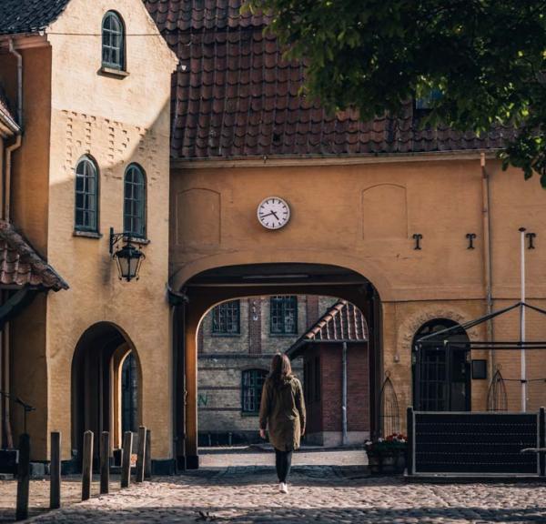 Kvinde på vej ind gennem port i gammel bygning i Assens. Uret over porten viser, at klokken er 17.45.