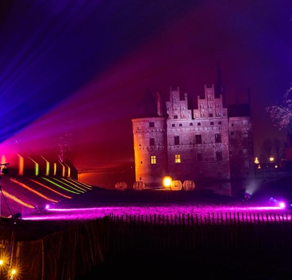 I baggrunden står Egeskov slot i mørket. Den lange græsplæne foran slottet er lyst op af forskellig farvede lamper. 