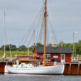 Flotte sejlskibe ligger til ved en havn med dansk flag.