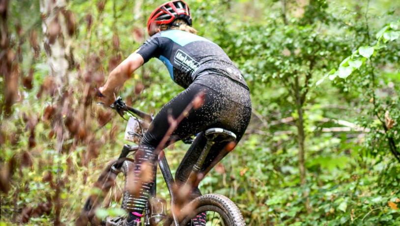 Mountainbiker med rød hjelm er til løb og cykler ude i skoven omringet af en masse grønt.