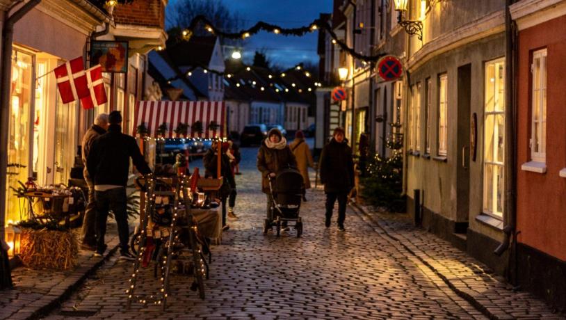 Julemarked i Ærøskøbing i skumringen med lyskæder, mennesker med varmt tøj på og varmt lys fra vinduerne.