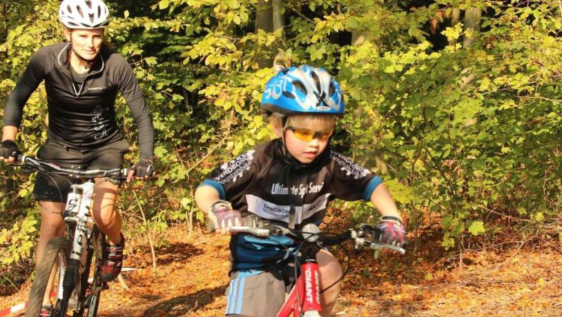 Kvinde og barn på mountainbike i skovterræn.