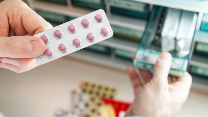 Hånd holder blisterpakke med piller, der er taget ud af medicinskab