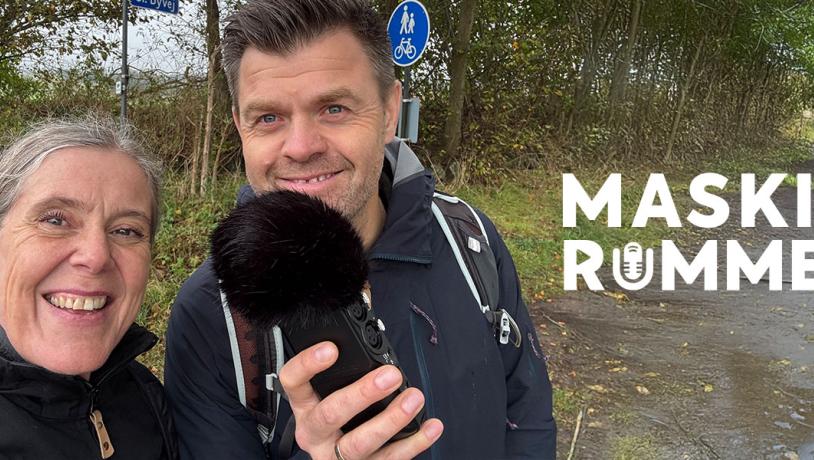 To personer i naturen, den ene holder en mikrofon. På billedet ses teksten Maskinrummet.