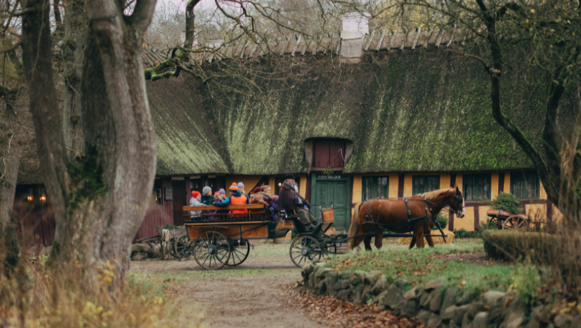 En familie kører i en gammeldags hestevogn igennem en gammeldags landsby om efteråret