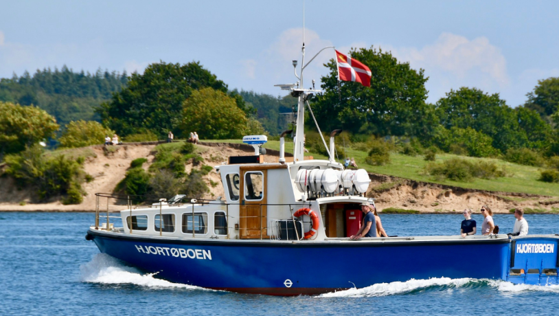 En blå mindre færge sejler forbi en skrænt med græs. 