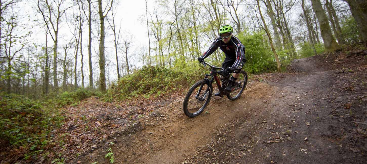 En mountainbiker med grøn hjelm cykler i skoven på vej ned ad en bakke.