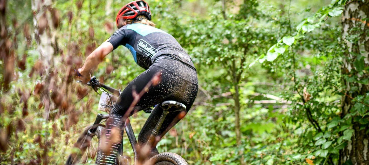 Mountainbiker med rød hjelm er til løb og cykler ude i skoven omringet af en masse grønt.