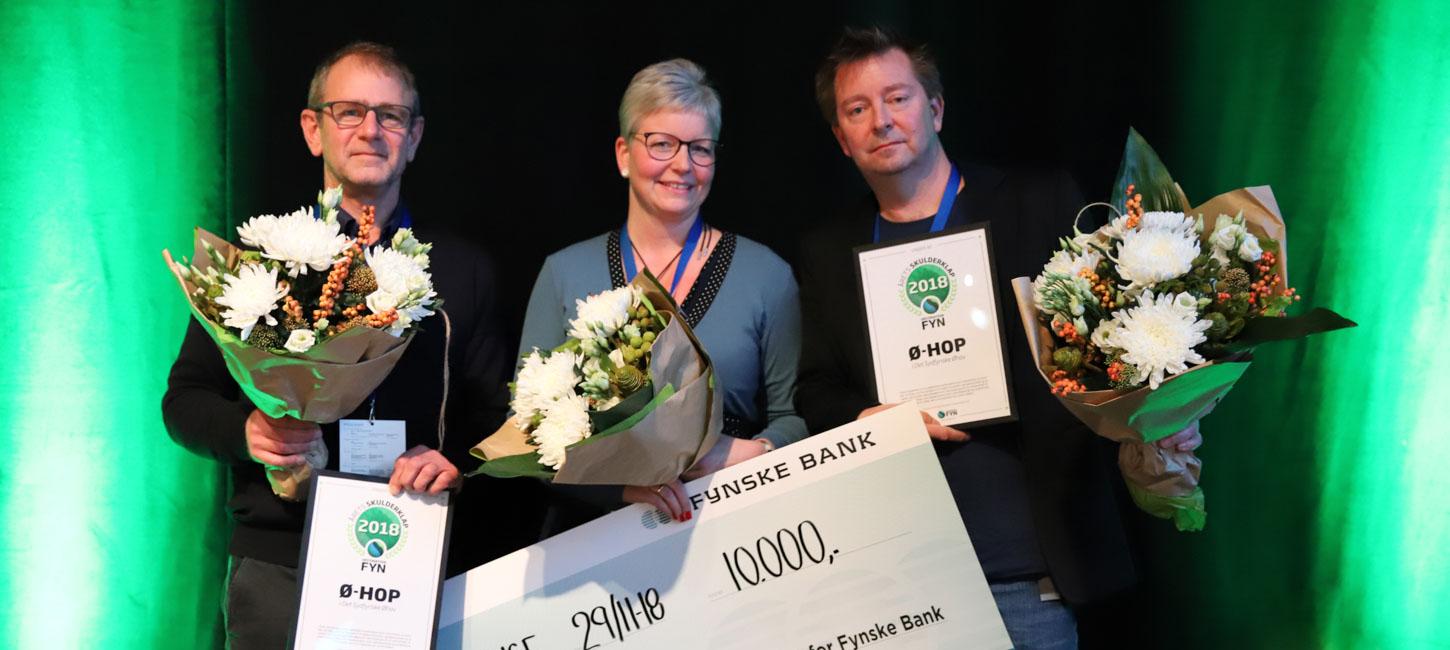 Tre personer med blomster på en scene, der har fået overrakt et gavekort på 10.000 kr.