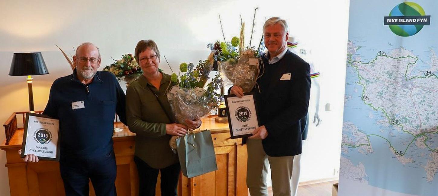 Tre glade modtagere af Bike Island-prisen på Fyn 2019 står med deres overrakte blomster og diplom.