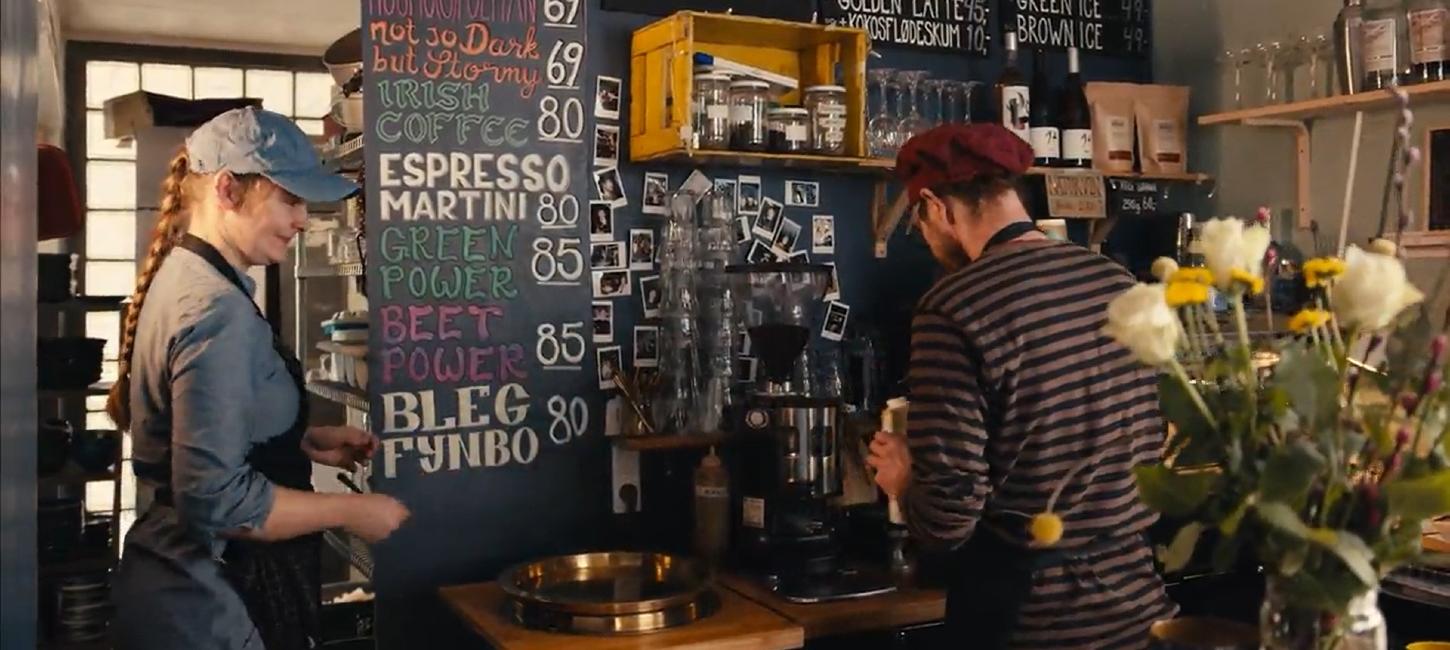 Bag disken på en café står en mand med ryggen til og laver kaffe.