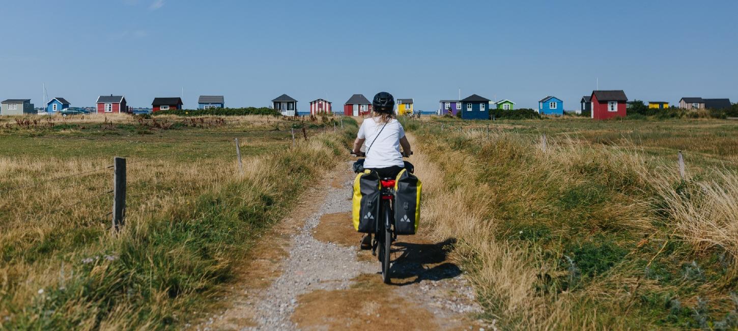 Kvindelig cyklist ses bagfra på vej ud til badehusene ved Vester Strand på Ærø. Det er sommer.