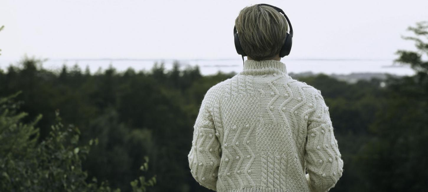 Person, der kigger ud over naturen ses bagfra med høretelefoner på
