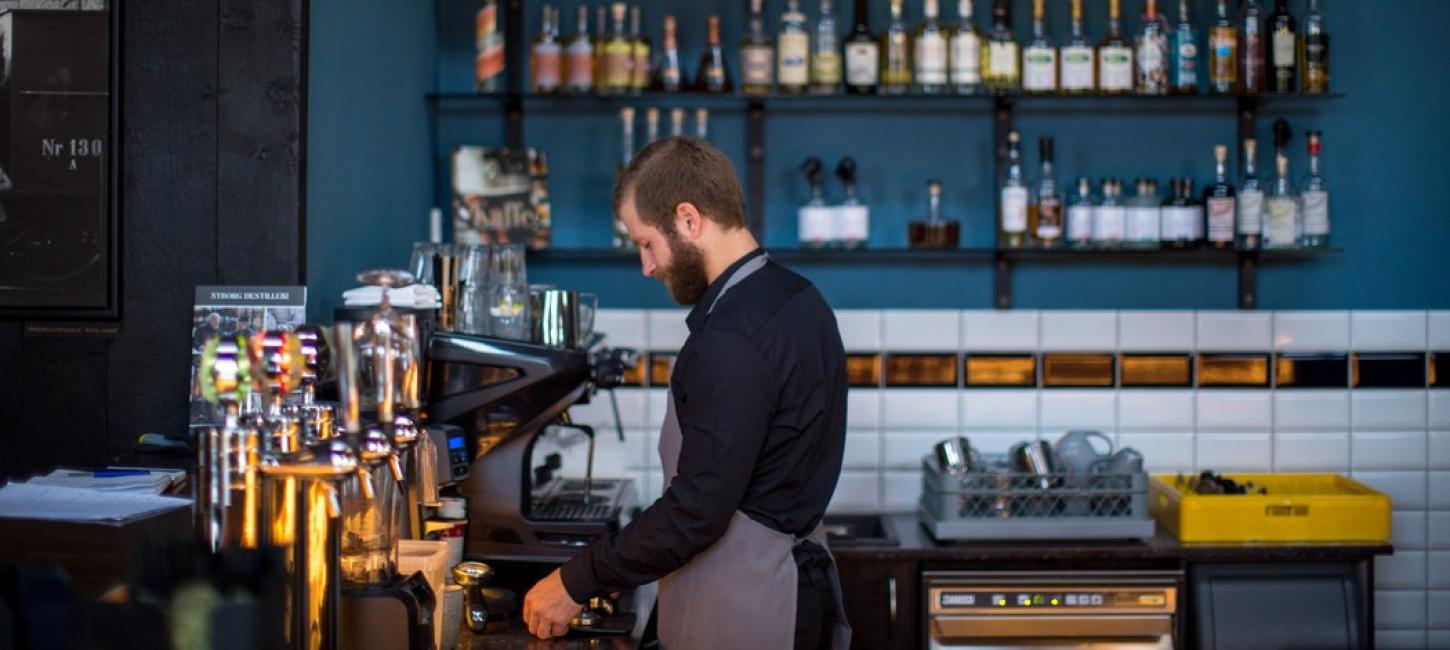 En mandlig barista står bag baren på en restaurant.