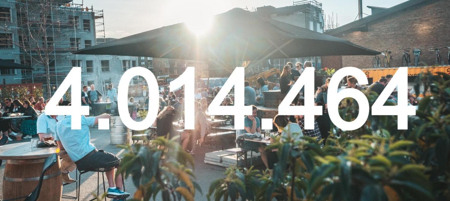 Mennesker er samlet ude foran Storms Pakhus i Odense en solskinsdag. I forgrunden kan man se tallet '4.014.464', som er Fyns opnåede historiske overnatningstal i 2021.