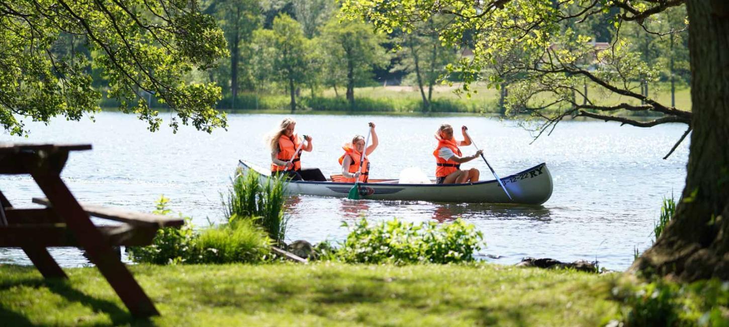Tre mennesker med hver deres åre sejler i kano på en solskinsdag.
