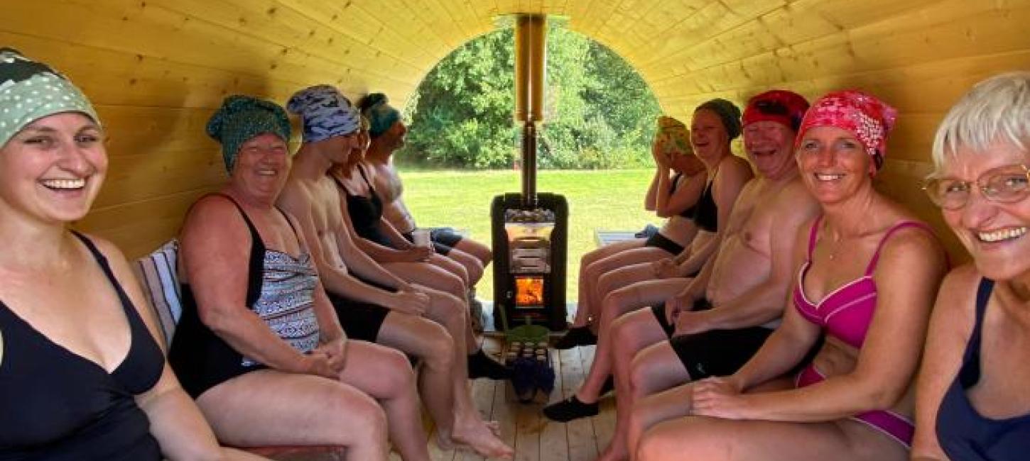 En flok glade mennesker sidder bænket på ræd og række i en træbeklædt sauna
