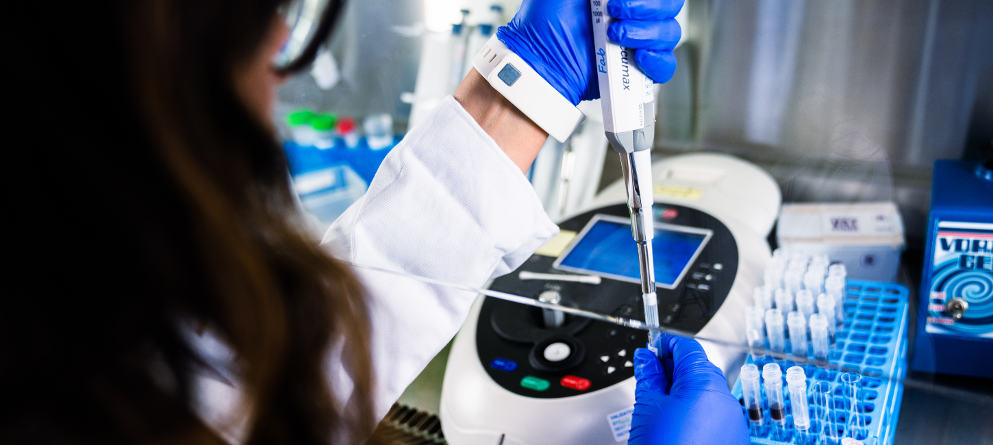 Hænder med blå engangshandsker injicerer i reagensglas