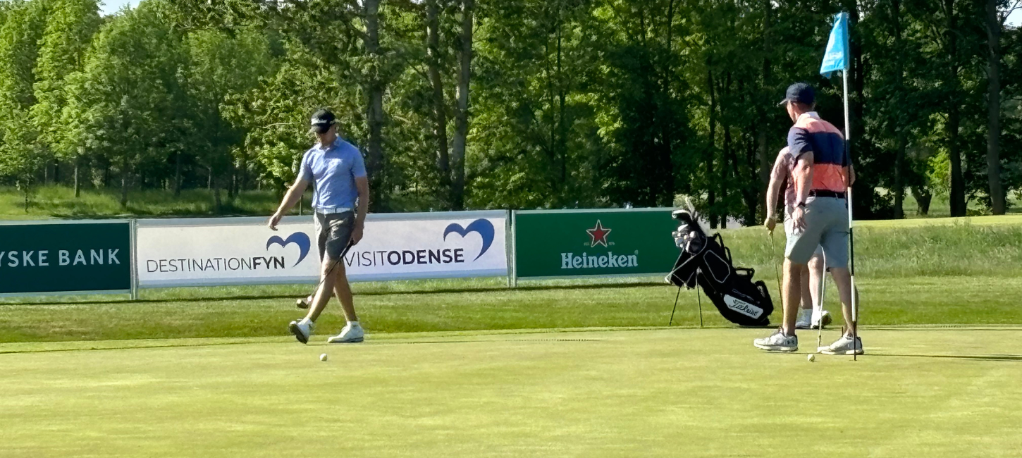 Golfspillere på golfbane med bannere i baggrunden