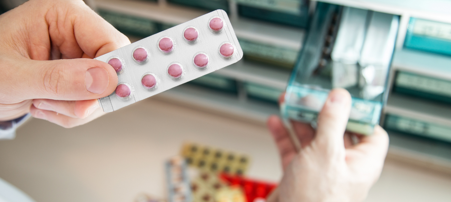 Hånd holder blisterpakke med piller, der er taget ud af medicinskab