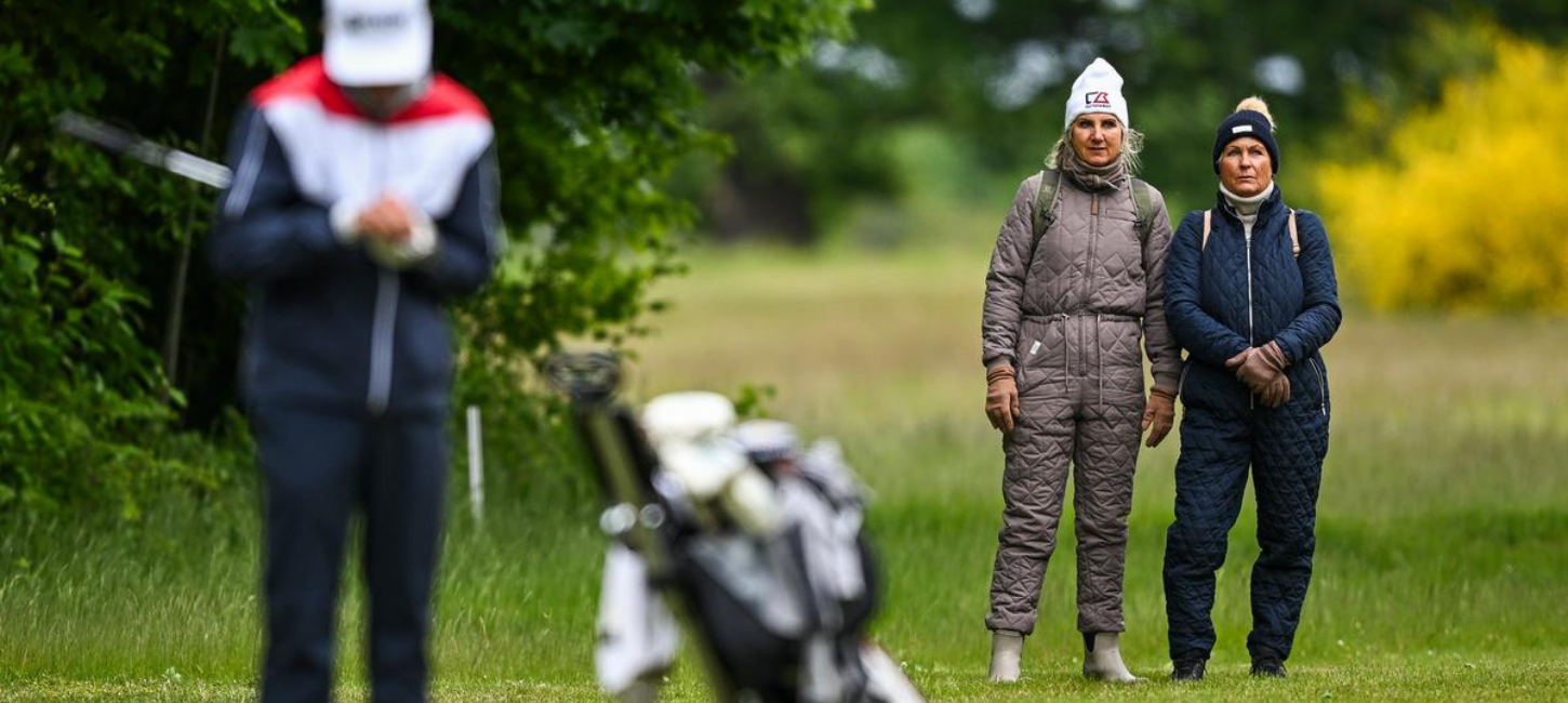 To kvinder står og kigger på en golfspiller