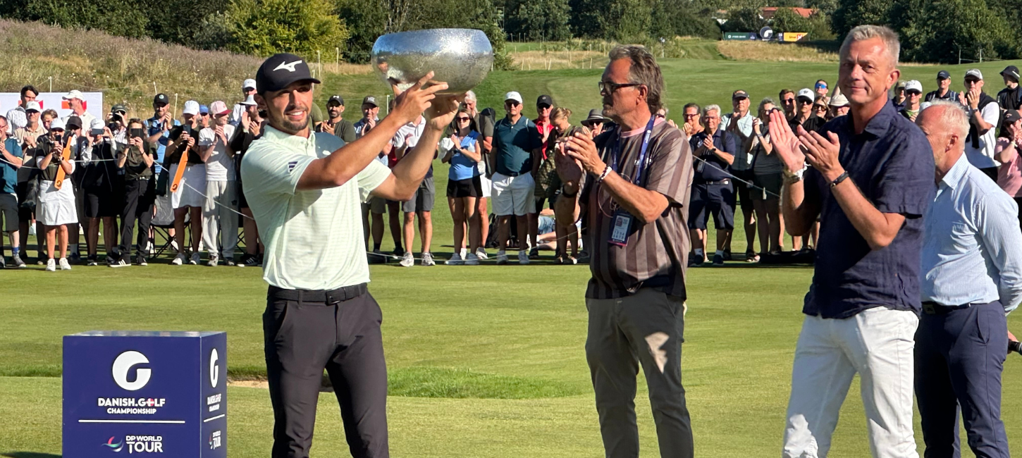 Golfspiller løfter stort trofæ, og folk omkring ham klapper
