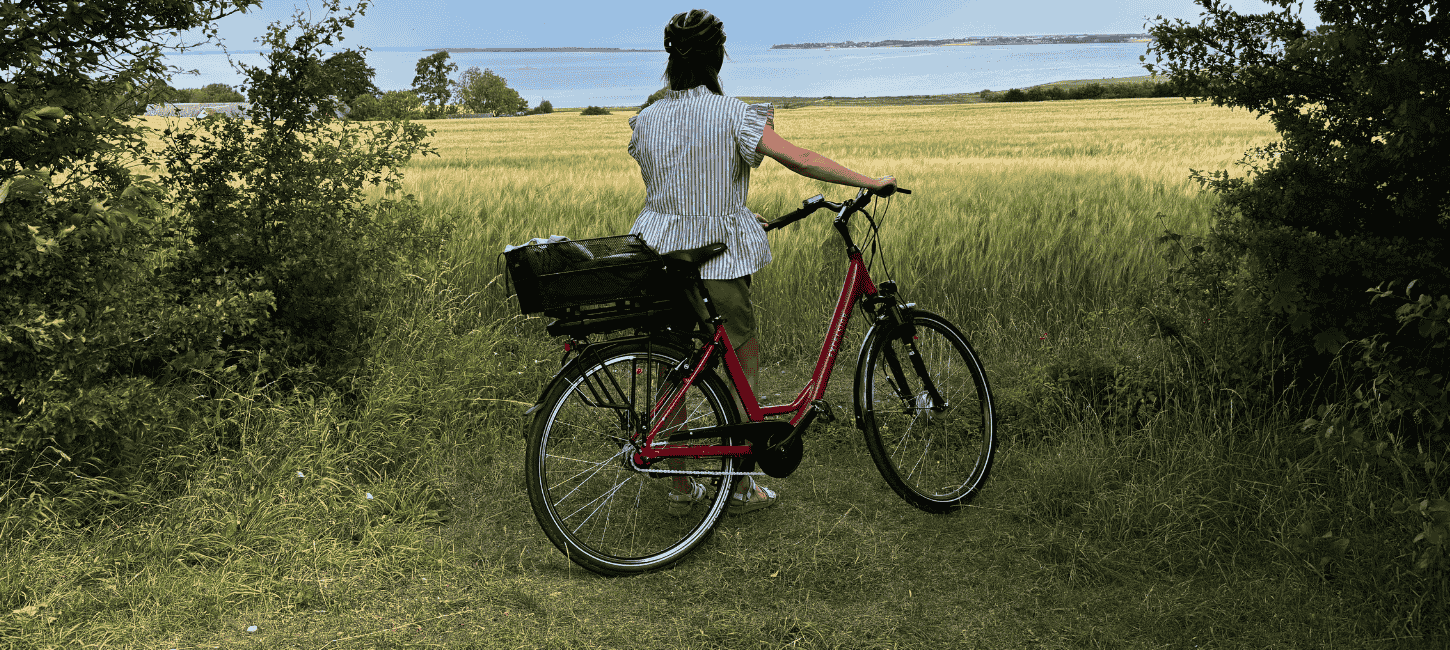 En cyklist står ved siden af en cykel og kigger ud over en mark med havet i horisonten