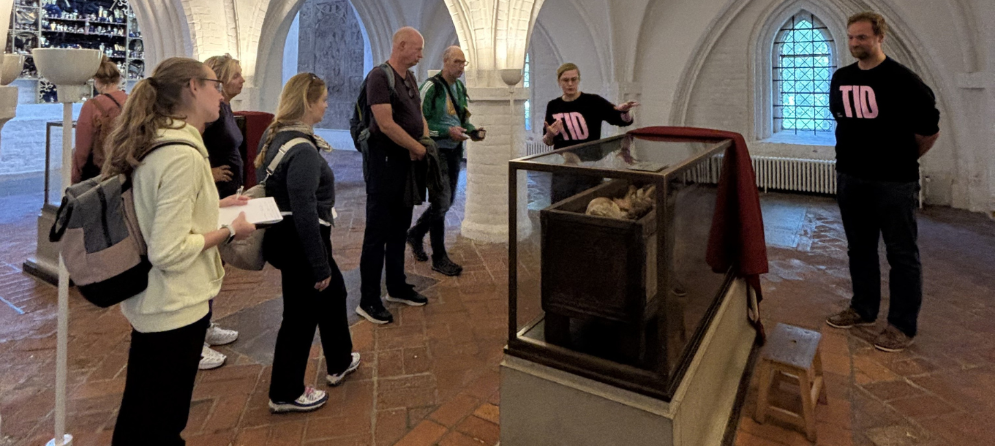 Besøgende og to rundvisere fra TID foran glasmontre.