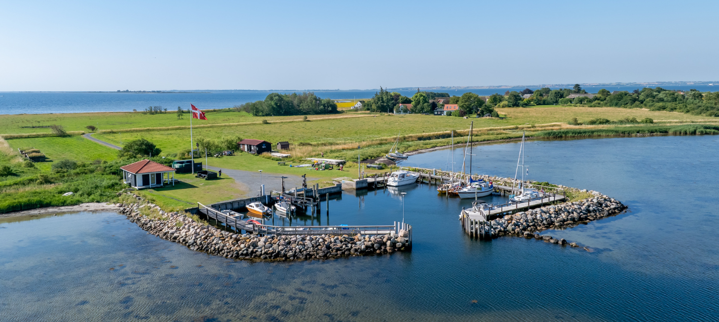 Dronebillede af Hjortø. Øen er både omgivet af blåt vand og himmel. 