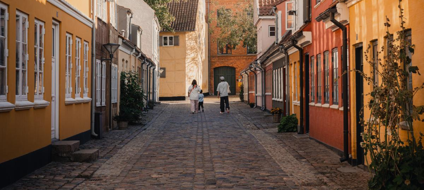 Tre personer går ned ad brostensbelagt gade med farverige husfacader