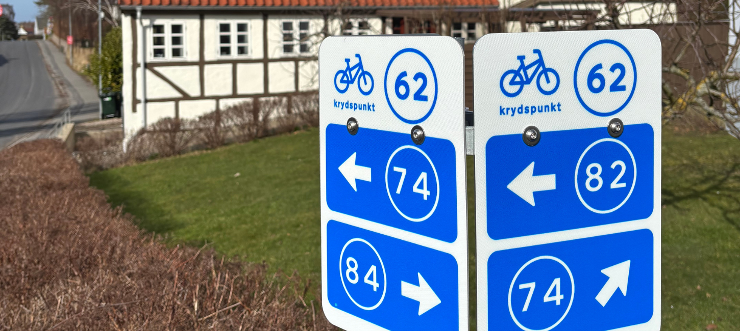 Cykelnetskilte på Langeland med bindingsværkshus i baggrunden