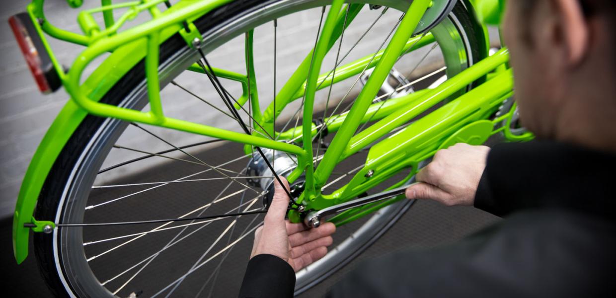 Close-up af baghjulet på en lysegrøn cykel, der bliver spændt efter af mand, som anes i forgrunden.