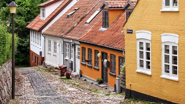 Gamle byhuse i orange og hvide farver på skrånende brostensbelagt gade i Assens