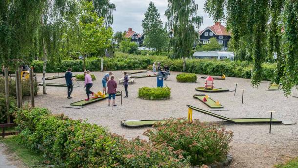 Man ser ind på en minigolfbane. Den består af grus og et flertal af små grønne baner hvor der går folk rundt 