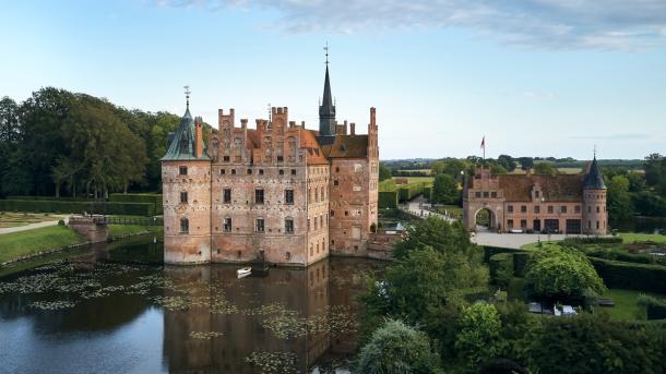 Egeskov Slot set fra oven med vandet foran og en åben blå himmel i baggrunden.