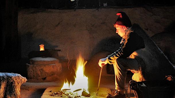 En mand med nissehue sidder foran et bål og kigger på ilden. 