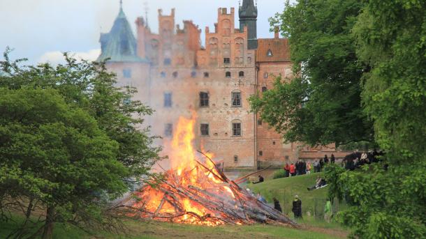 Egeskov i baggrunden, et skt hans bål i forgrunden omkranset af grønne buskadser og træer