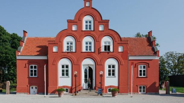 Rød bygning med hvide vinduer og hvidt hegn.