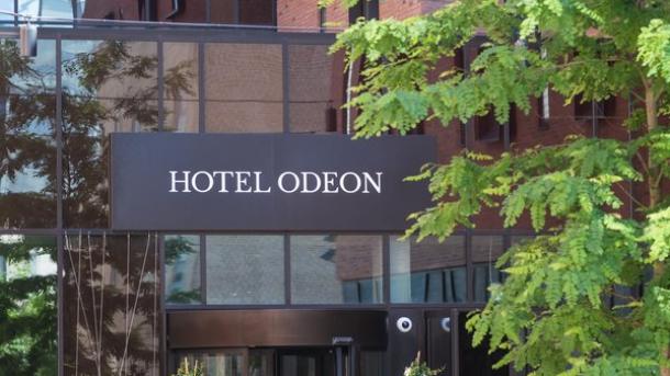 En facade på hotel med grønne træer ved siden af indgangspartiet