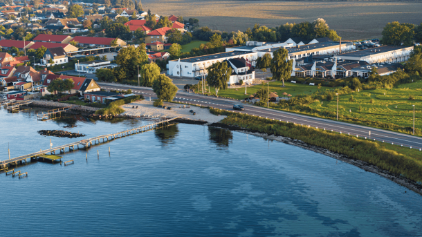 Dronefoto af hotel lige ud til kysten med grønt græs, blåt hav og et rødt svajende dannebrog
