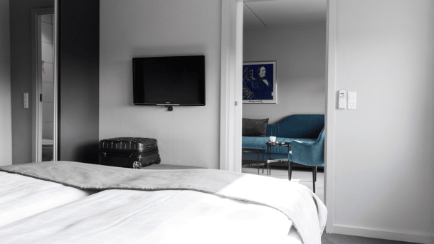 Hotelværelse med dobbeltseng, tv på væggen og et tilstødende stue-rum