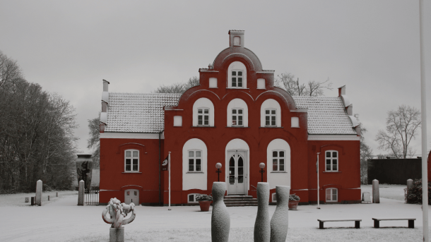 En rød herregård iklædt sne med skulpturer foran