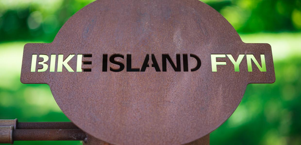 Close-up af rustfarvet skilt med teksten Bike Island Fyn. 