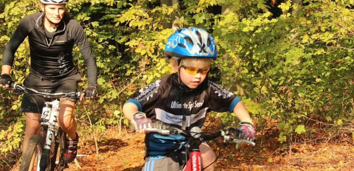 Kvinde og barn på mountainbike i skovterræn.