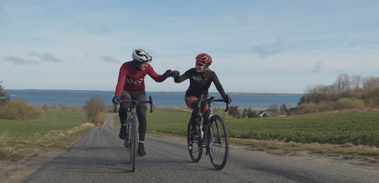 Et par cykler op ad en bakke på landevejen og holder i hånd.