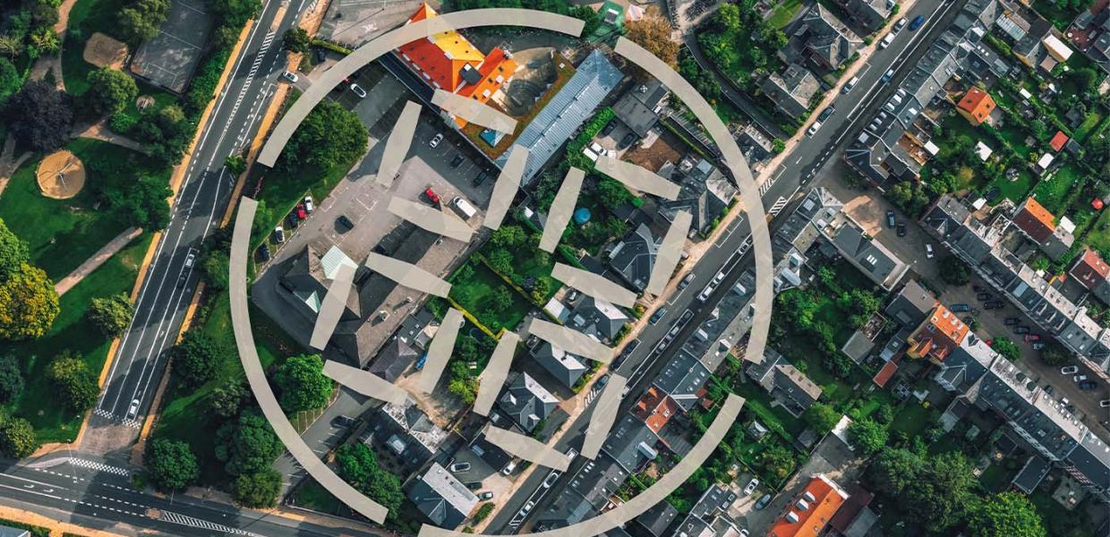 Luftfotografi af en by med grå og røde tage, lige veje og grønne områder.