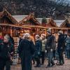 En brostensplads er fyldt med mennesker pakket ind i vintertøj. Rundt om pladsen står små træhytter pyntet med gran og julelys. Træhytterne har en åben front som giver adgang til de juleting de sælger. 