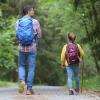 En mand og en pige vandrer med rygsække langs en sti i en grøn skov